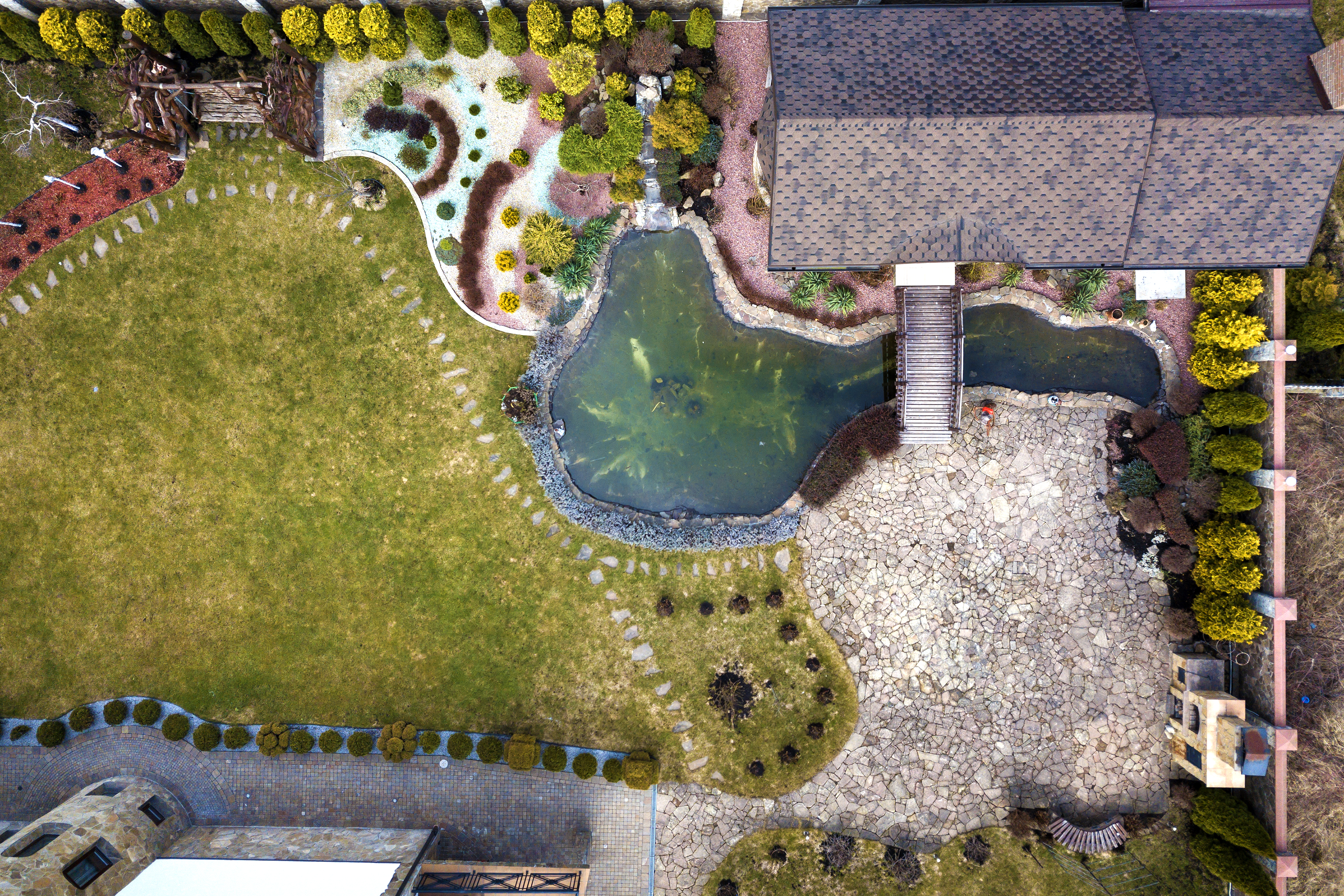 Aerial view of beautifully landscaped property complex. Roofs of recreation house cottage, pond in ecological area on bright sunny day. Modern architecture, landscaping concept.